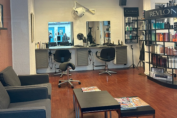Bilde av salongen, med behagelige sittestoler og ventestoler. Rekkverk med sjampoer, hårfarge og andre produkter. Behagelig atmosfære.